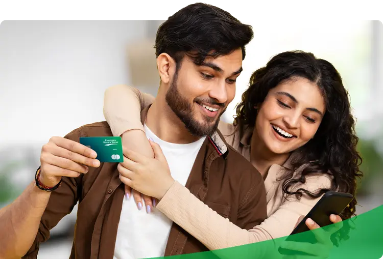 Smiling couple managing their finances with a debit card and smartphone—showcasing the convenience of checking and savings accounts that keep your money at work in the local community.
