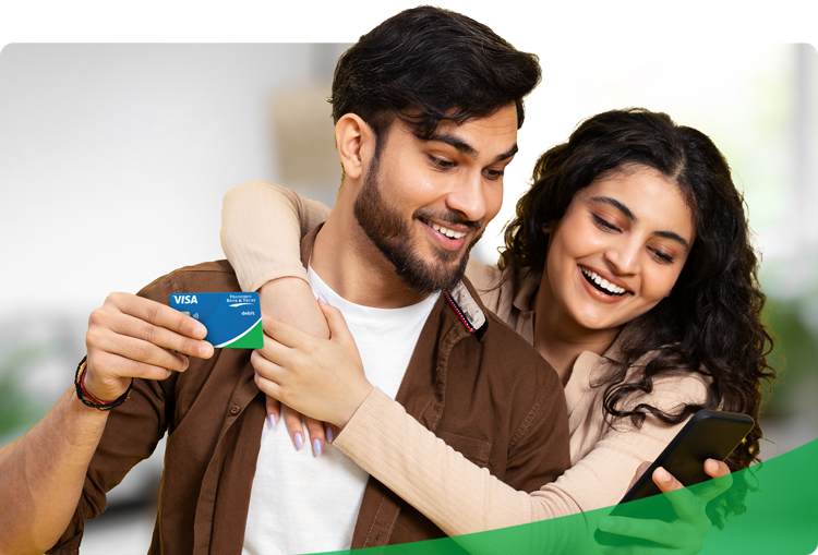 Smiling couple managing their finances with a debit card and smartphone—showcasing the convenience of checking and savings accounts that keep your money at work in the local community.